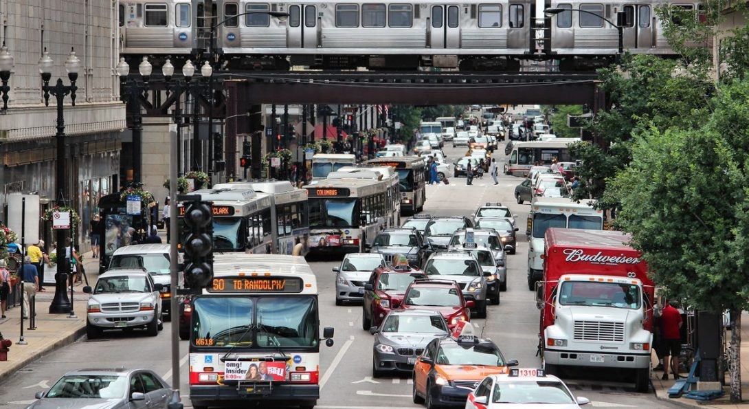 Busy street in Chicago with cars and a CTA bus traveling below an elevated train bridge with an L train.