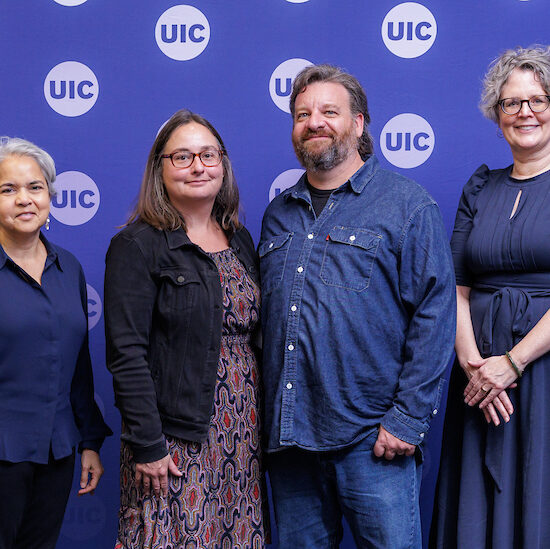 four individuals stand in front of a blue backdrop that has the UIC circle logo
