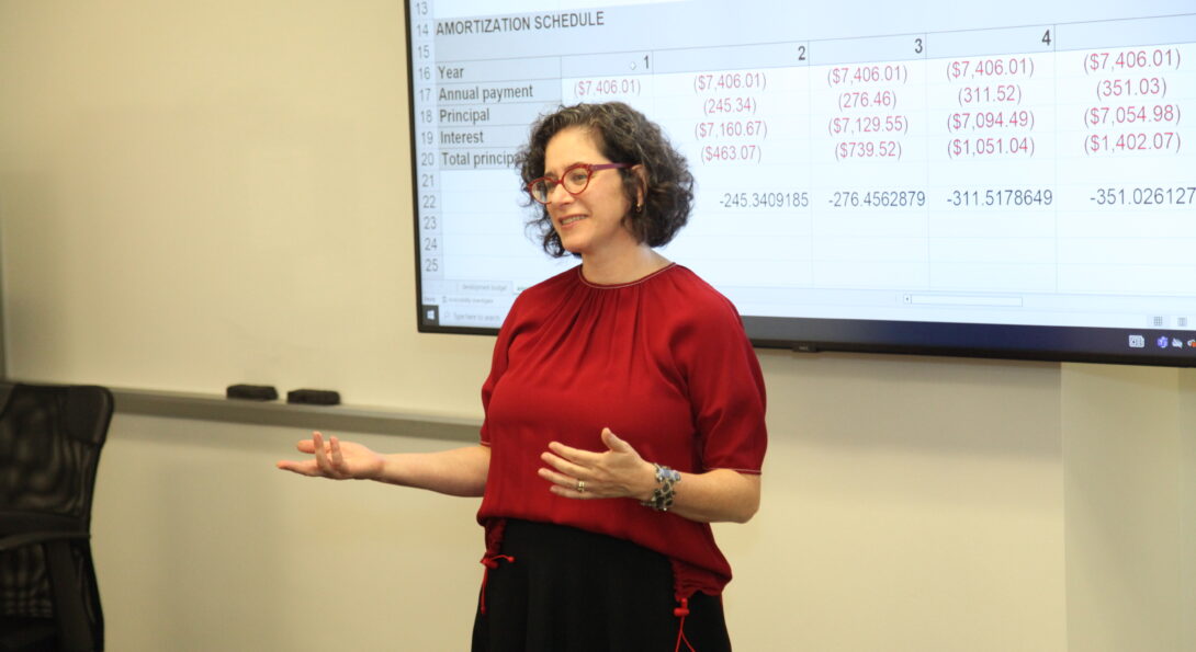 Urban planning and policy professor, Rachel Weber, in red shirt in front of a screen with a development finance spreadsheet in the classroom