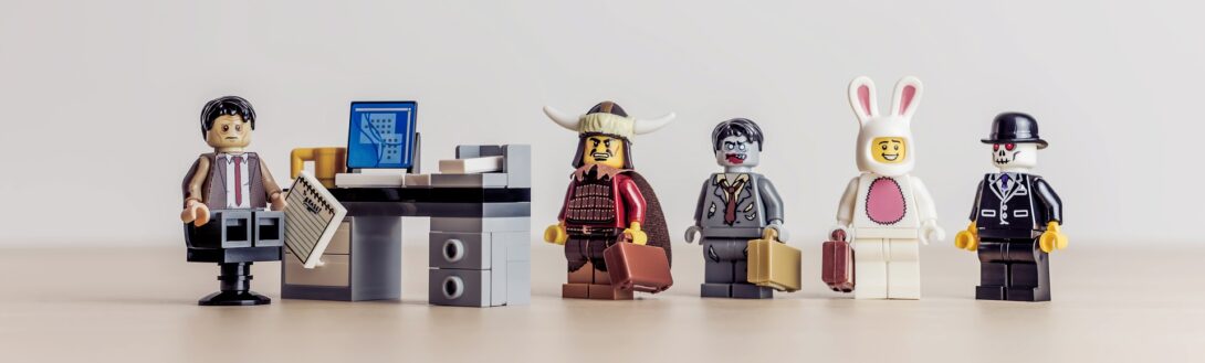 A lego businessman at his desk with four mini figs dressed as a Viking, a business person, a bunny, and a suited gentleman.