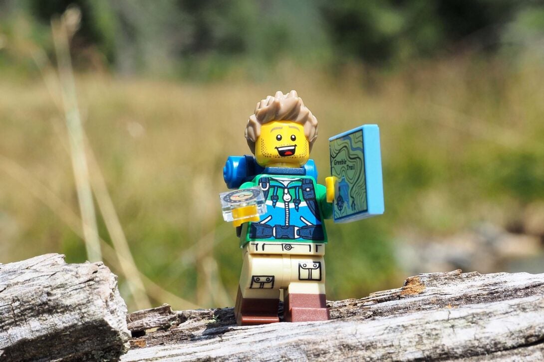 Lego figure in the woods with a map and an compass in his hand.