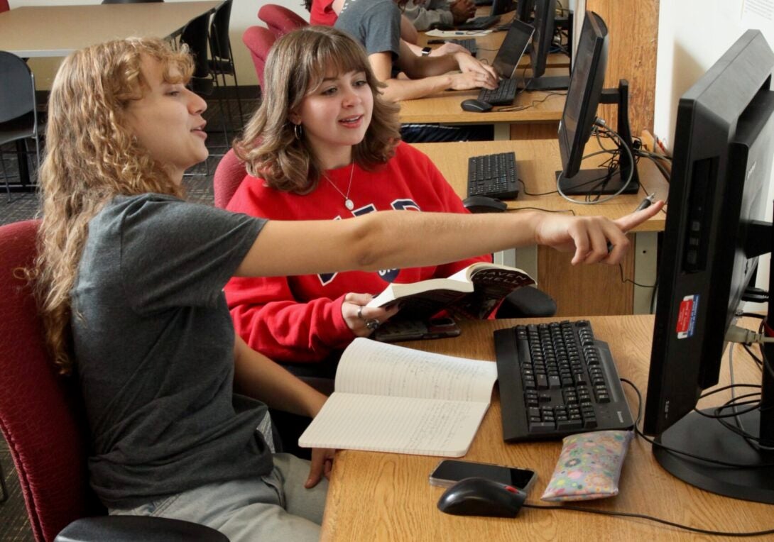 Two students in UIC tee-shirts work together at a computer.