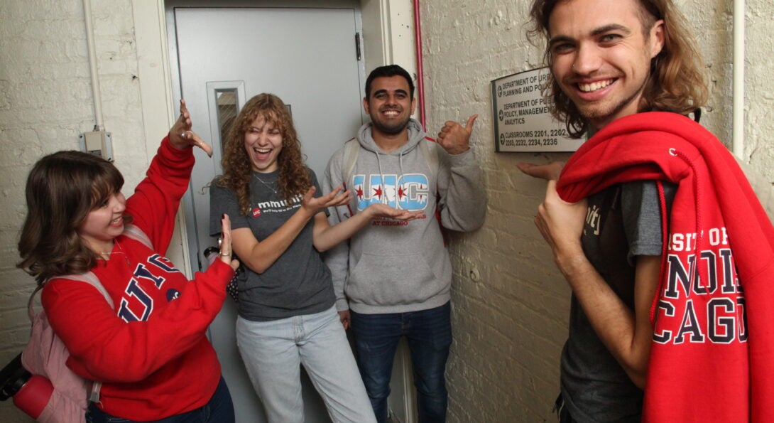 Four CUPPA students stand in the building stairwell pointing to signage leading to the academic departments.