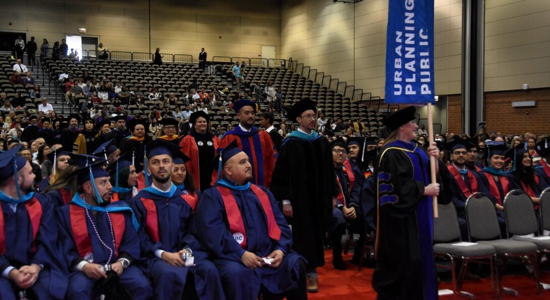 CUPPA Faculty in academic regalia processing in with a blue CUPPA tall banner during the 2024 May commencement ceremony.