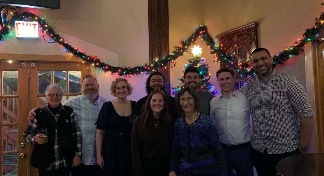 Nine CUPPA Alumni Board members pose with green holiday decorations and lights.