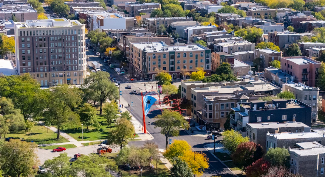 Photo of west side Chicago neighborhood with trees, green grass, and both tall and medium size brick buildings.