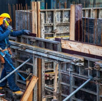 A construction worker in blue overalls works on the exterior frame of a building.
                  